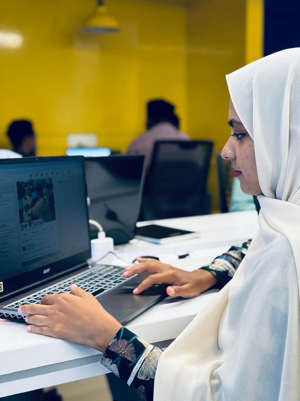 Suhaila V.M, a digital marketing freelancer, focused on her laptop while working on a campaign in a modern, brightly-lit office.
