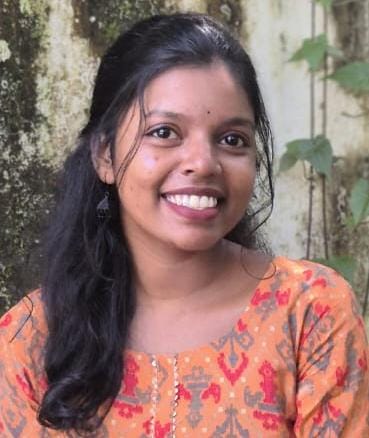 Professional portrait of Anusree, Managing Director, smiling and wearing an orange patterned kurta, with a natural, leafy background.