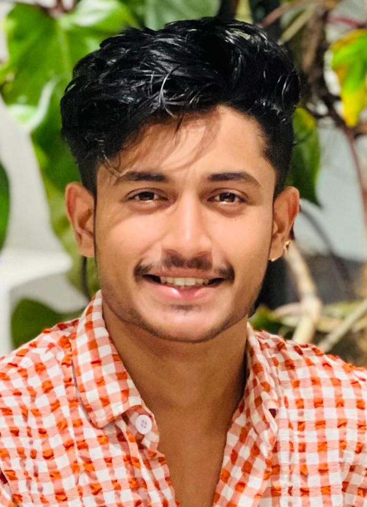 Professional headshot of Sejad M.P., Co-Founder of CHA, smiling and wearing an orange and white checkered shirt, with green foliage slightly visible in the background.